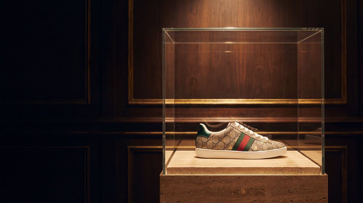 NAHJ The Icons banner v2 — sneaker in museum glass vitrine on travertine (desktop)